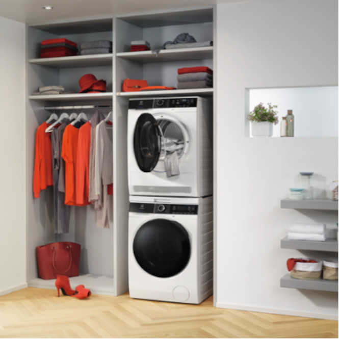 Beyaz dolapta çamaşır ve kurutma makinesi, raflarda giysiler, kırmızı çanta ve ayakkabılar var.