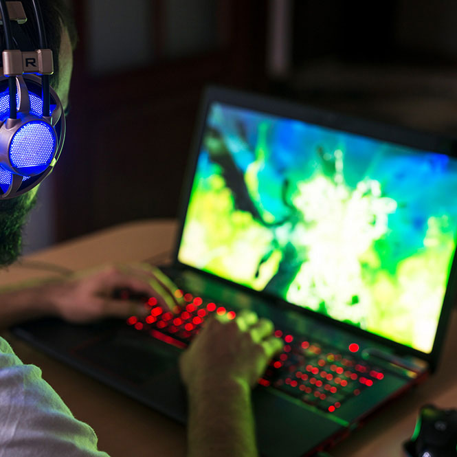 Kulaklıklı bir kişi, aydınlatmalı klavyeli bir dizüstü bilgisayarda yazıyor. Ekranda renkli bir görüntü var.